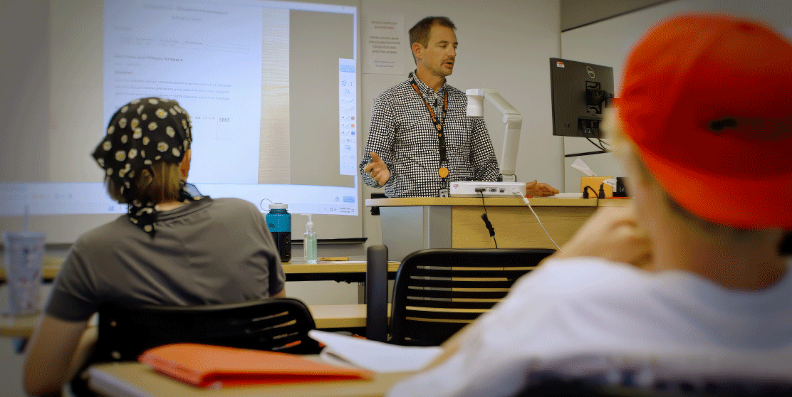 a teacher at a podium speaking to students in a classroom