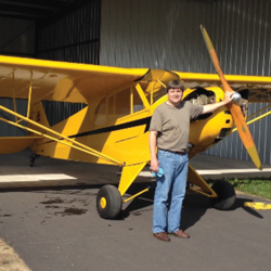 Glenn Rizner standing in front of a yellow GA plane