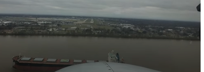 Picture showing tall ship within approach end of the runway with airplane flying over it on final.