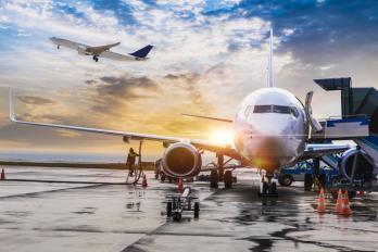 plane sitting on runway with plane taking off in background