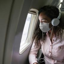 Woman with headphones and mask looking out an airplane window
